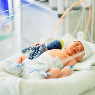 A baby in a hospital bed with an IV tube and bandaged limbs. 